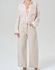 Person wearing a cream button-up shirt and beige pants on a white background