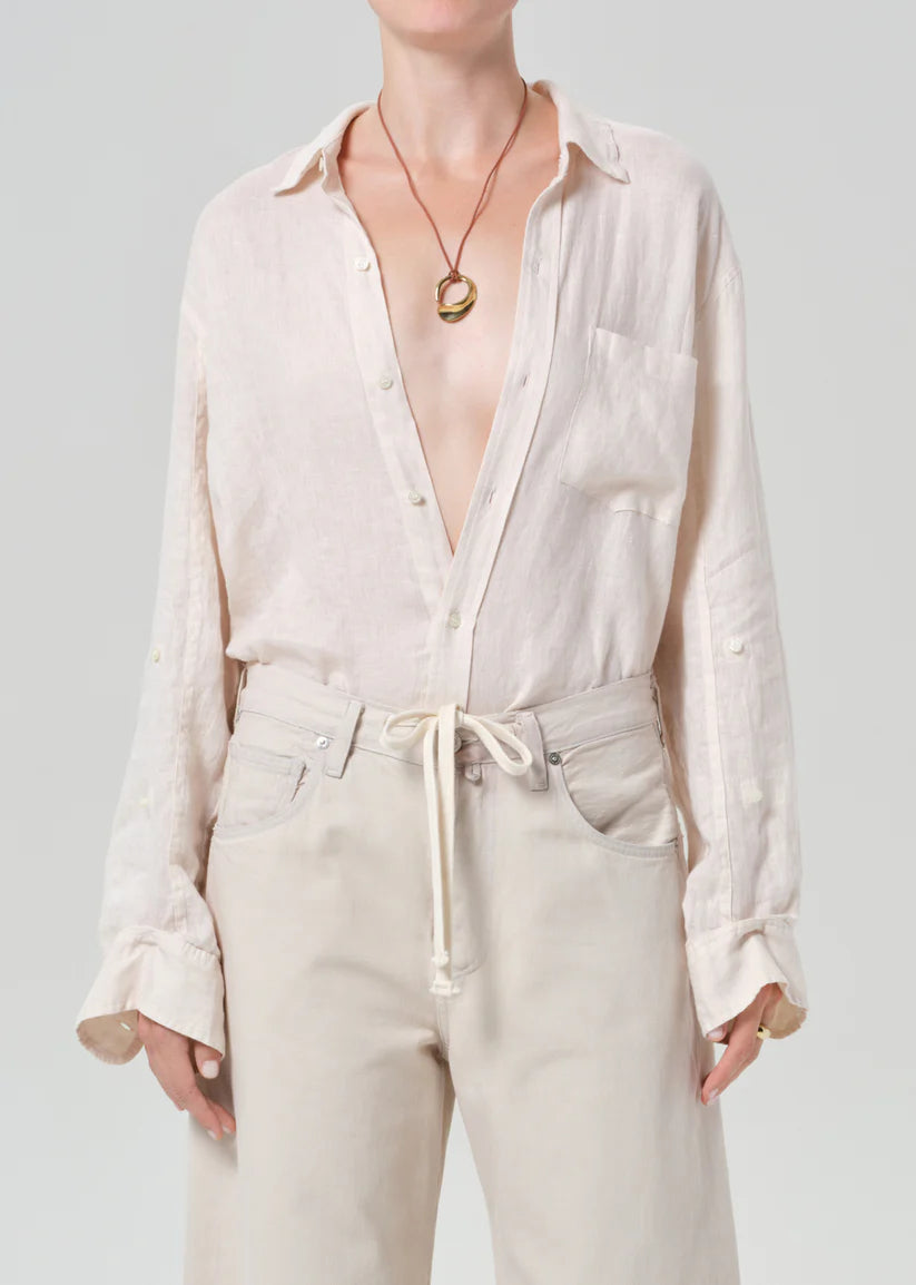 Person wearing a light cream button-up shirt and beige pants on a plain background