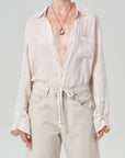 Person wearing a light cream button-up shirt and beige pants on a plain background