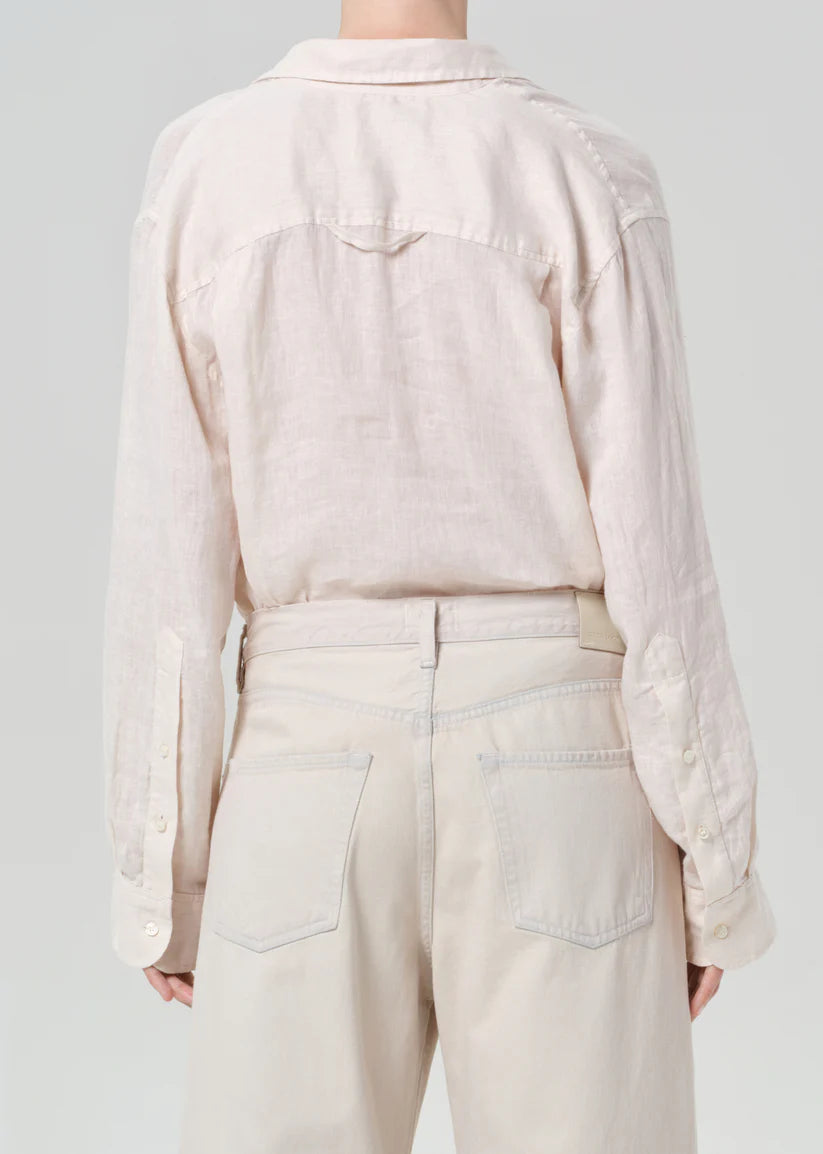 Person wearing a light cream shirt and beige pants against a gray background
