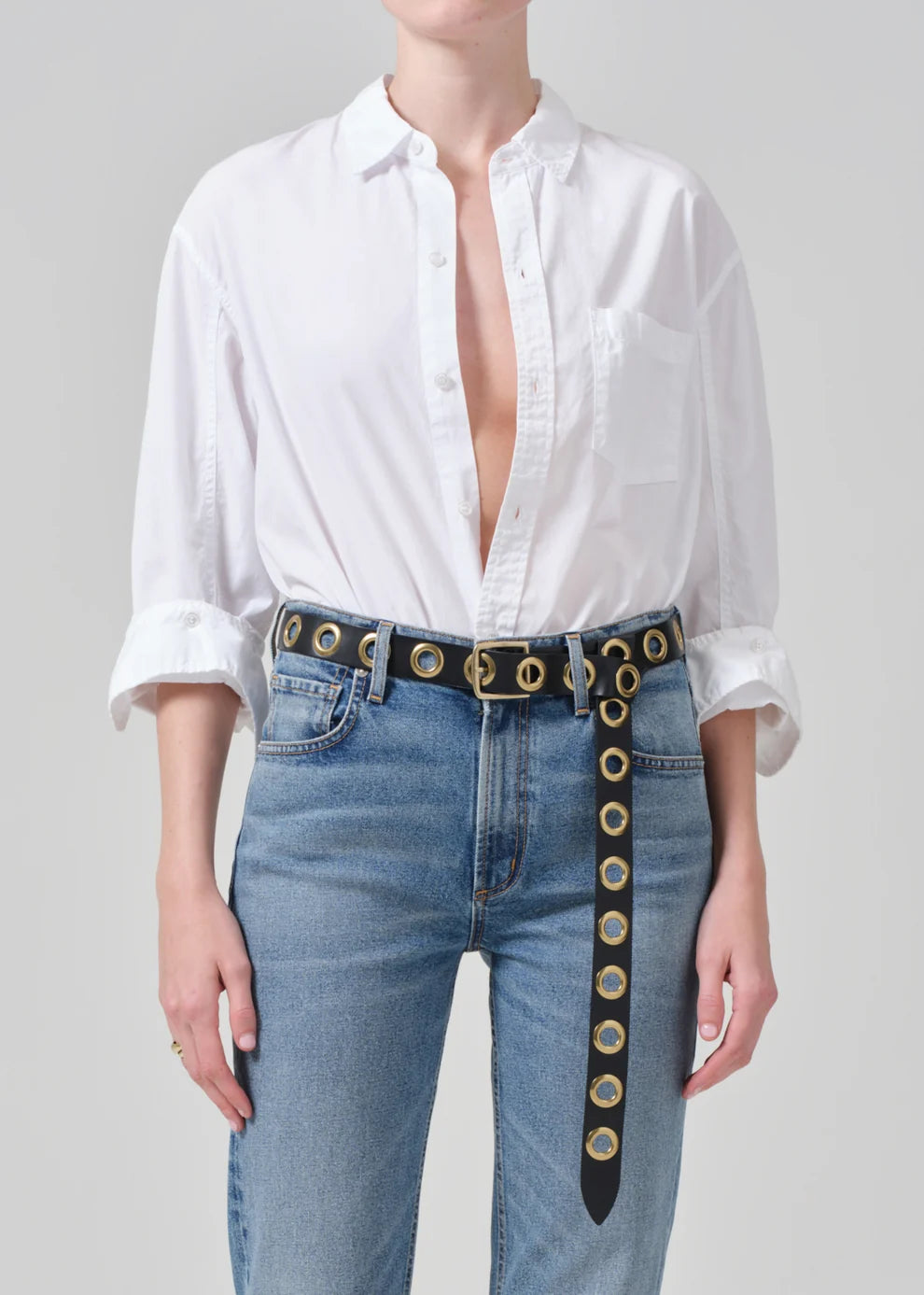 Person wearing a white shirt and blue jeans with a decorative belt on a gray background