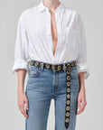 Person wearing a white shirt and blue jeans with a decorative belt on a gray background