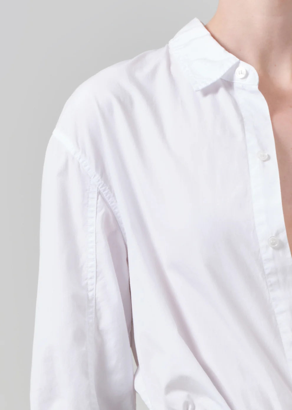 A close-up of a person wearing a white long-sleeve button-up shirt against a light gray background.