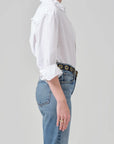 Person wearing a white shirt and blue jeans with a belt on a plain background