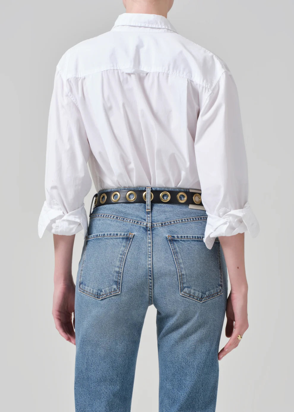 Person wearing a white shirt and blue jeans with a decorative belt on a plain background
