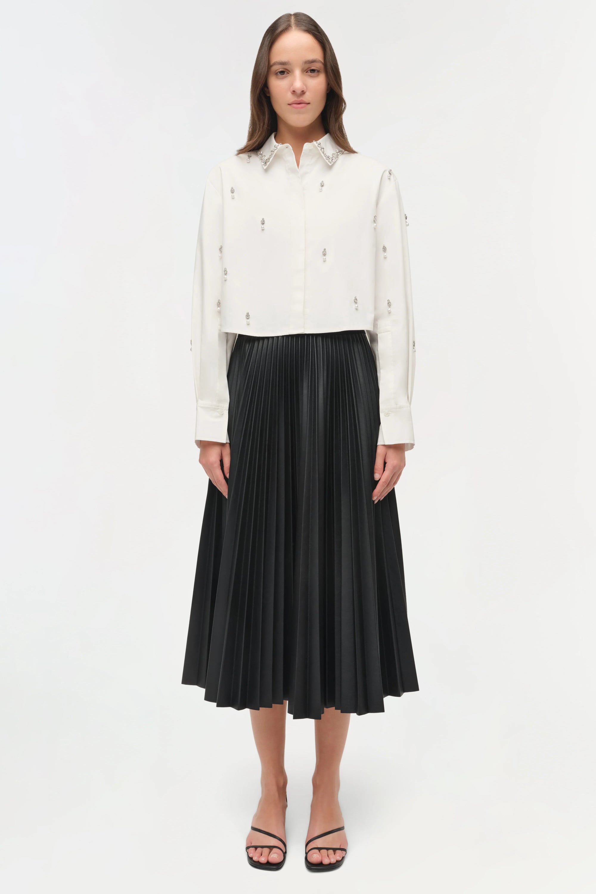 Woman wearing a white blouse and black pleated skirt on a white background
