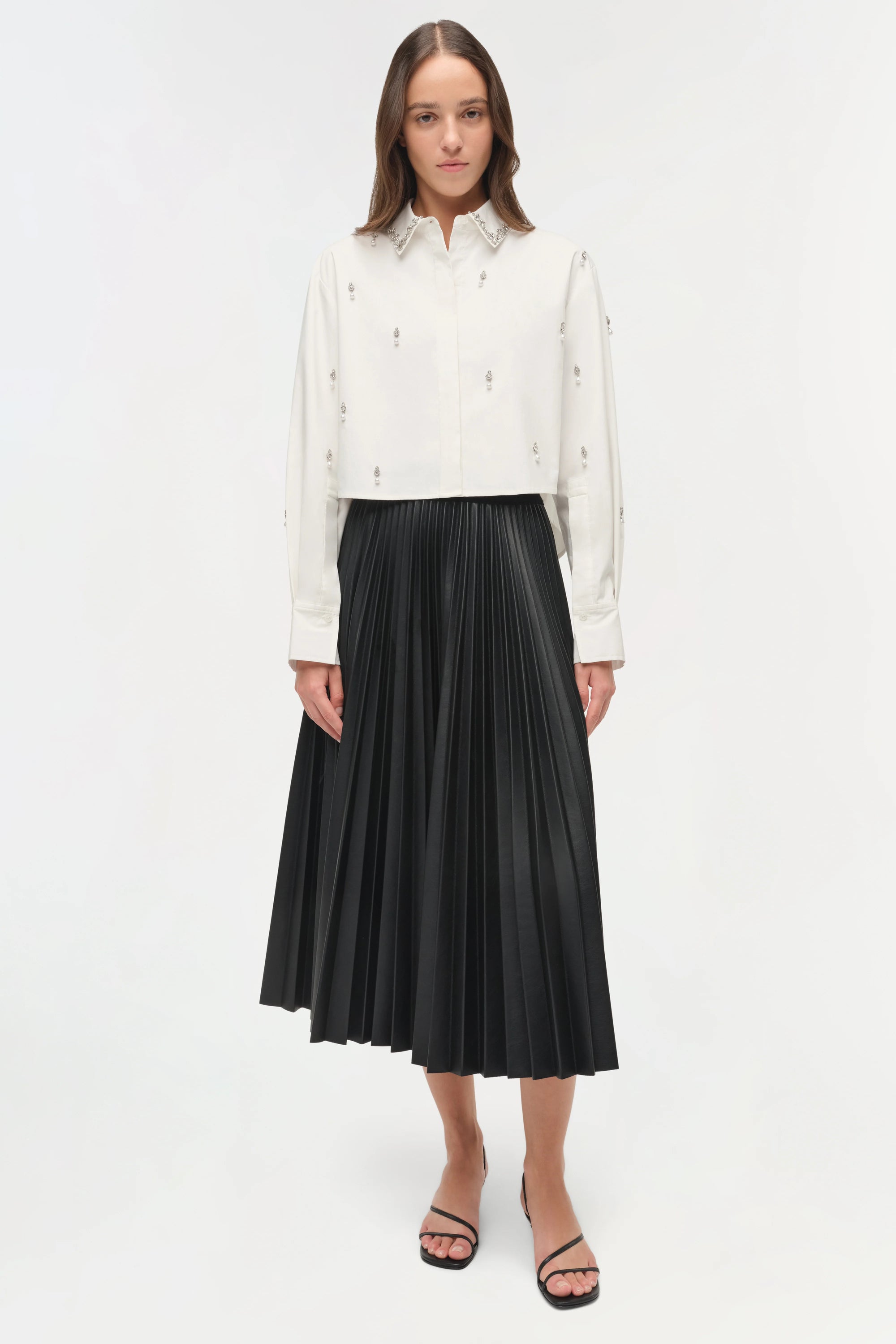 Woman wearing a white blouse and black pleated skirt on a white background