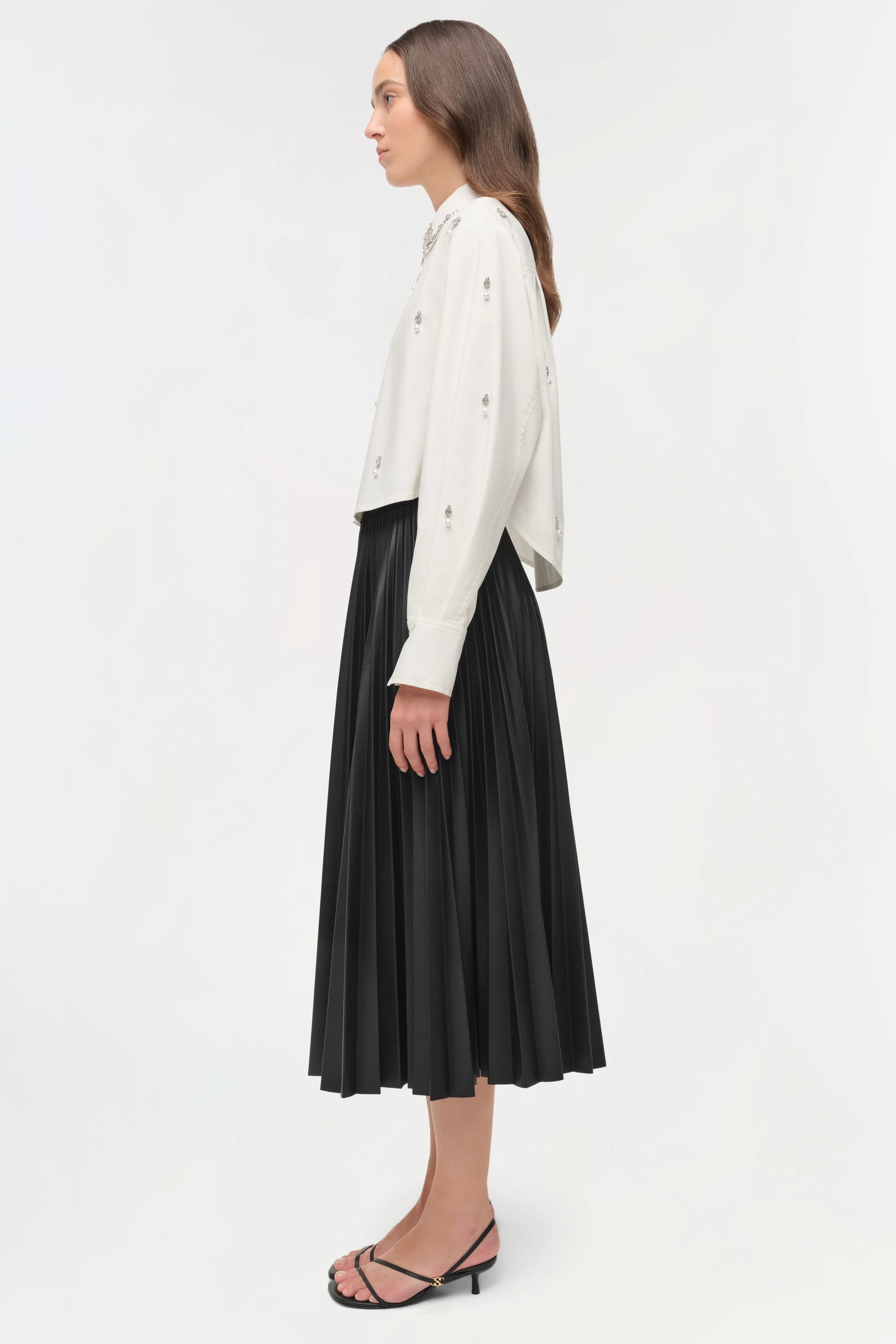 Woman wearing a white blouse and black pleated skirt on a white background