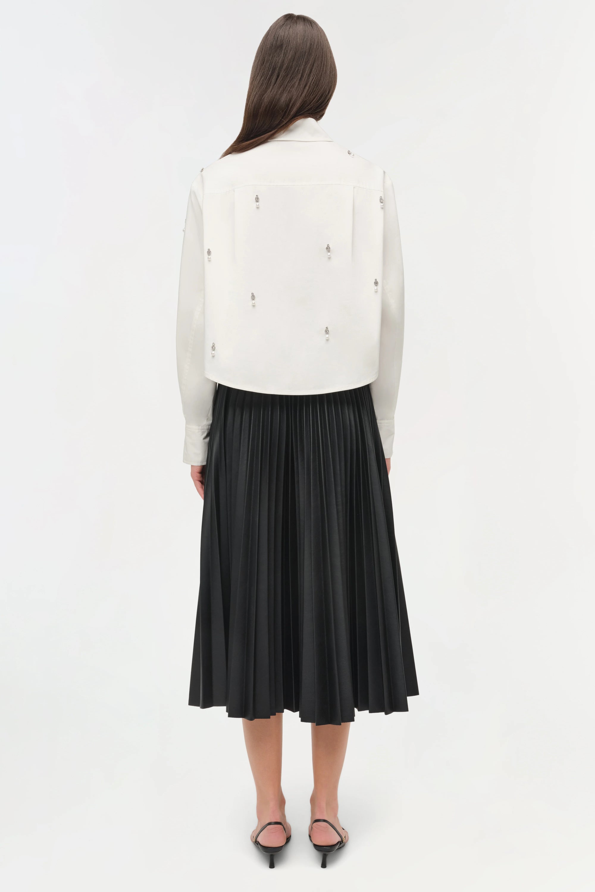 Person wearing a white jacket with black embellishments and a black pleated skirt on a white background