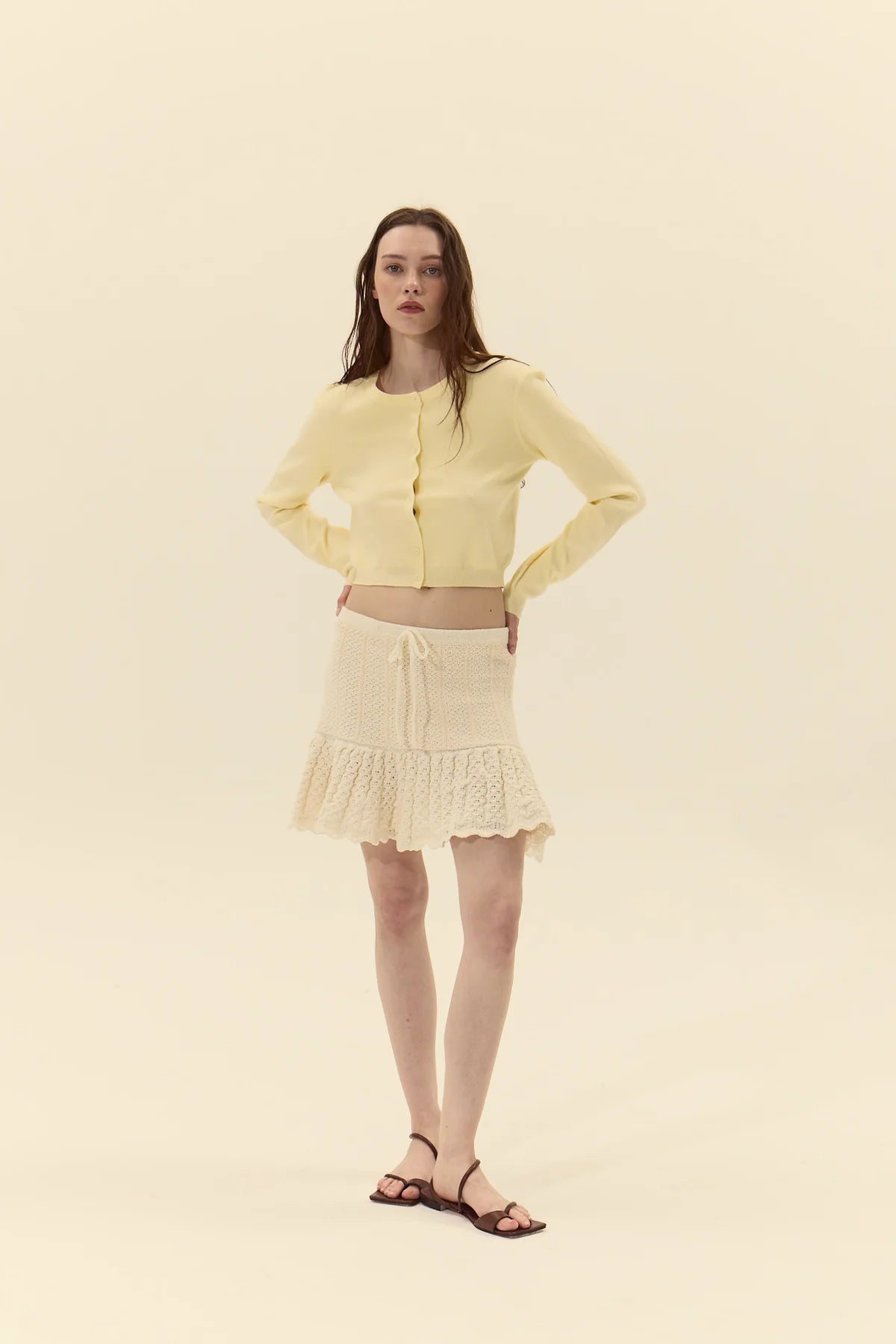 Woman wearing a yellow cardigan and skirt on a beige background