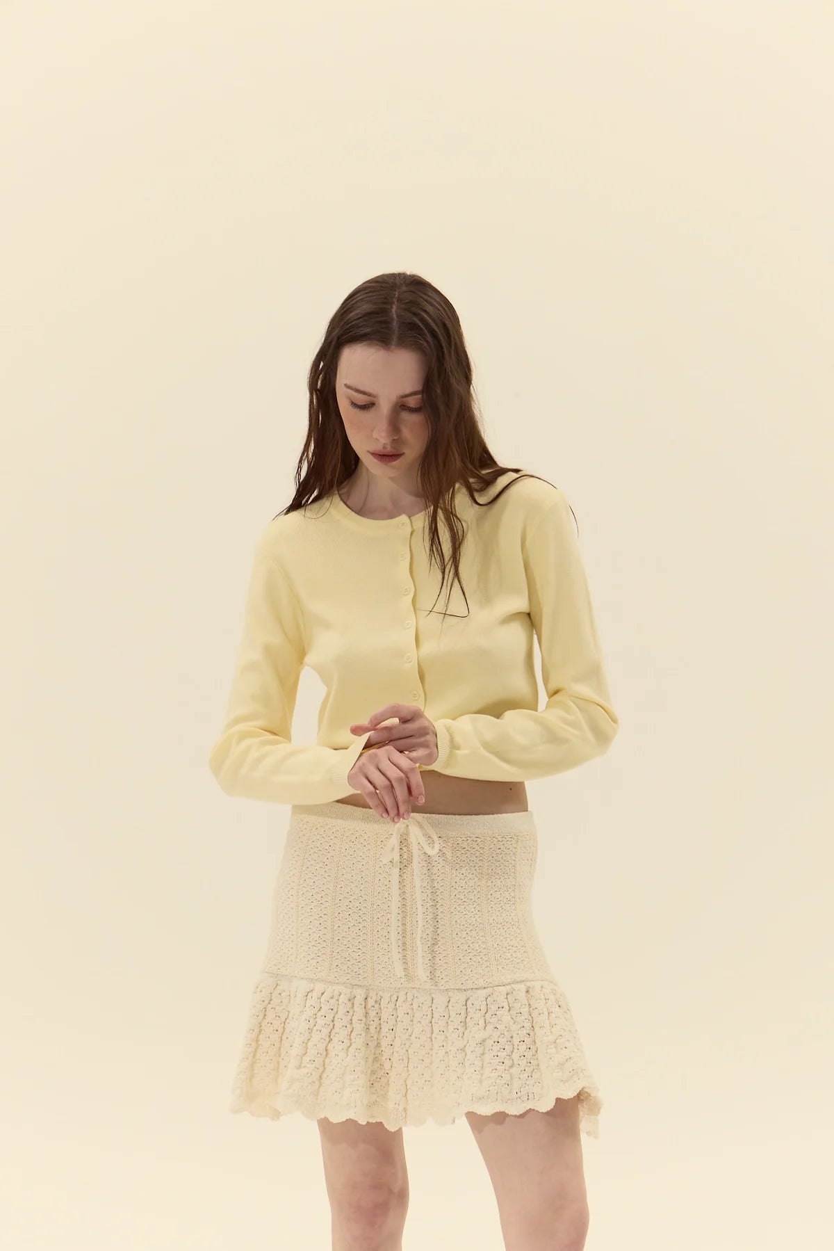 Woman wearing a light yellow outfit with a matching cardigan and skirt on a beige background