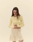 Woman wearing a light yellow outfit with a matching cardigan and skirt on a beige background