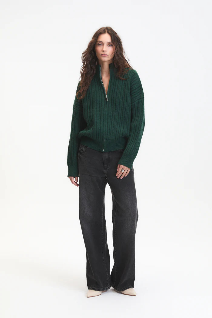 Woman wearing a green sweater and black pants on a white background