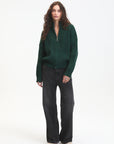 Woman wearing a green sweater and black pants on a white background