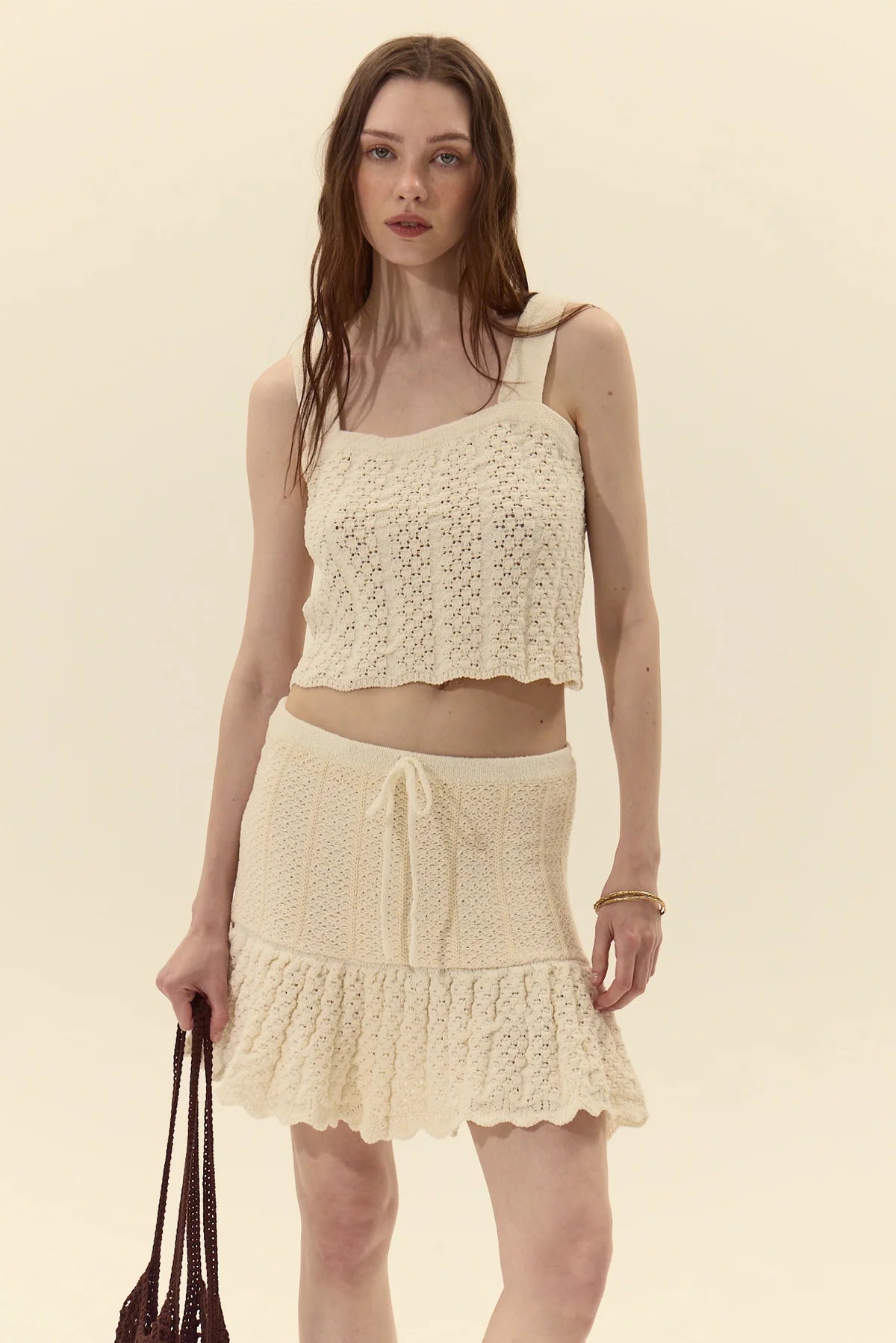 Woman wearing a cream-colored crochet top and skirt set on a beige background