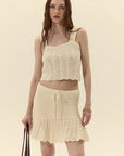 Woman wearing a cream-colored crochet top and skirt set on a beige background