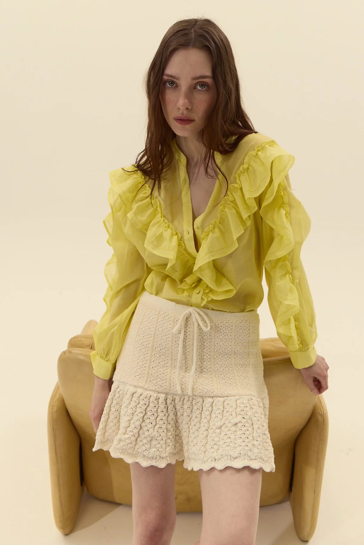 Woman wearing a yellow blouse and off-white knit skirt sitting on a beige chair.