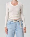 Person wearing a white long-sleeve top and light blue jeans with a belt on a gray background