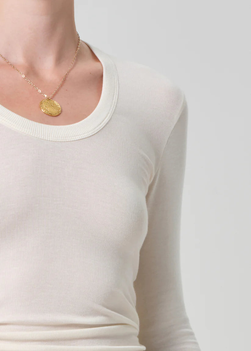 Person wearing a gold necklace with a pendant on a plain background