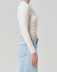 Person wearing a white long-sleeve top and light blue jeans on a plain background