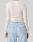 Person wearing a cream long-sleeve top and light blue jeans on a gray background