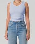 Person wearing a light blue tank top and high-waisted jeans on a plain background