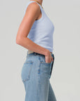 Person wearing a light blue tank top and light blue jeans on a plain background