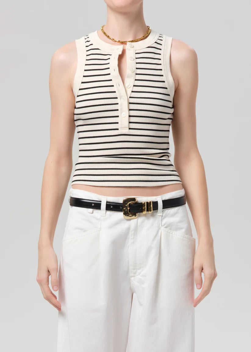 Person wearing a striped sleeveless top and white pants on a plain background