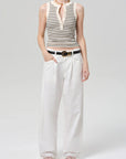 Person wearing a striped sleeveless top and white pants on a plain background