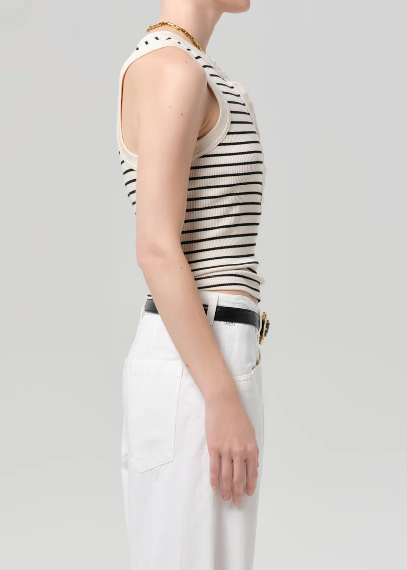 Person wearing a black and white striped tank top with white pants on a light gray background