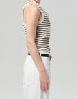Person wearing a black and white striped tank top with white pants on a light gray background