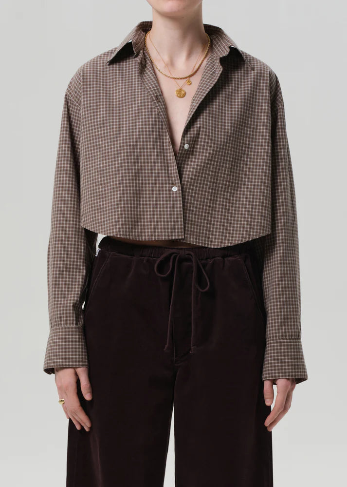 Person wearing a brown checkered shirt and dark pants on a plain background