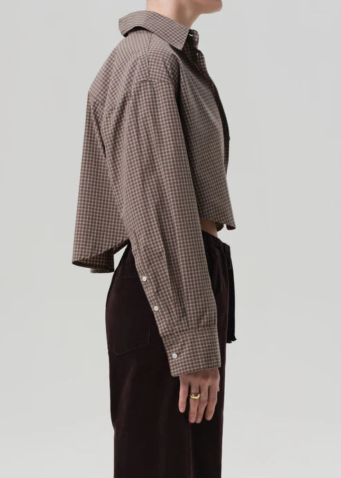 Person wearing a brown checkered shirt with a plain background, side