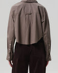 Person wearing a brown checkered shirt and dark pants on a light gray background, back