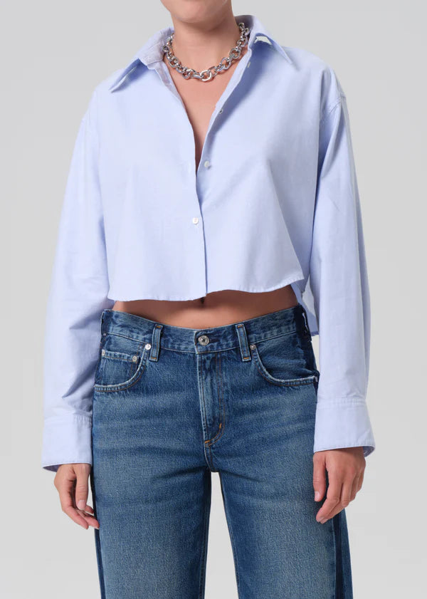 Person wearing a light blue button-up shirt and blue jeans on a plain background