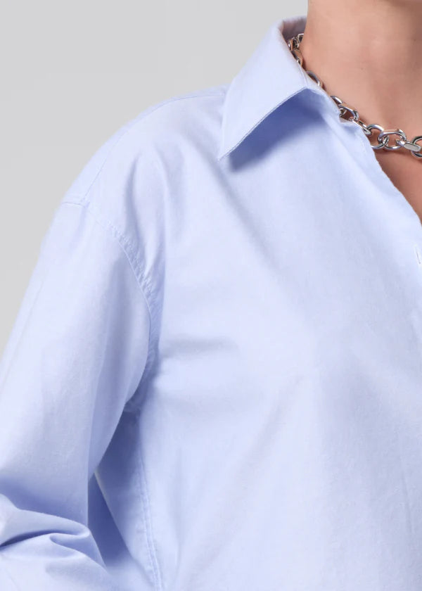 Close-up of a light blue shirt with a collar and a necklace on a neutral background