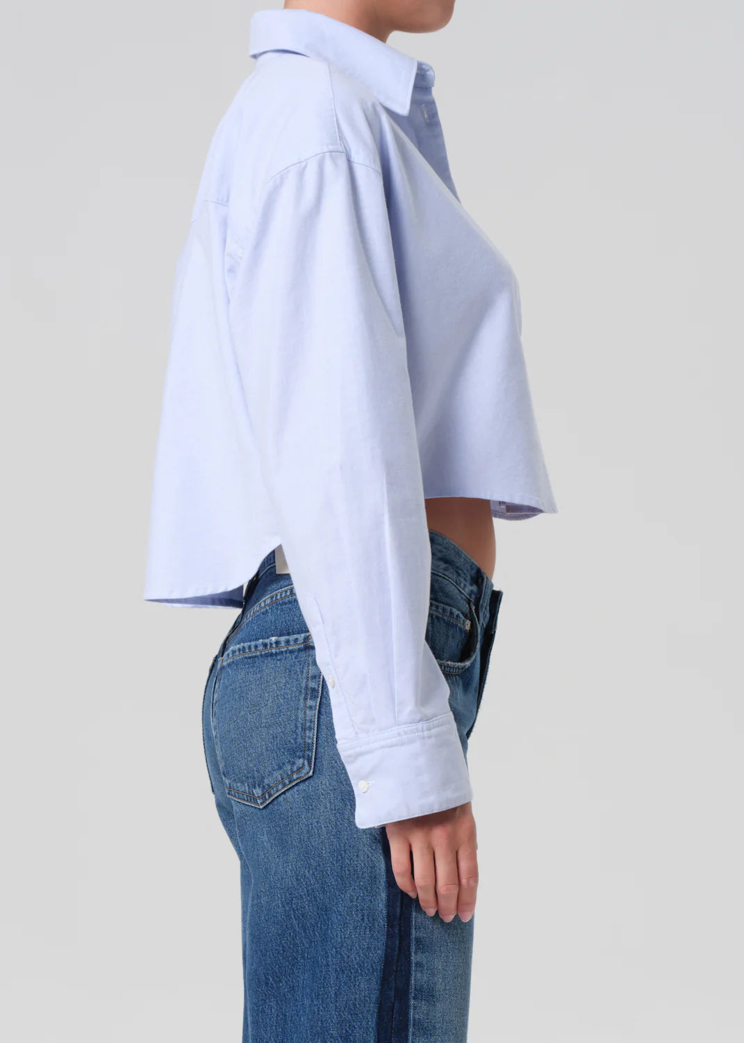 Person wearing a light blue shirt and jeans on a plain background