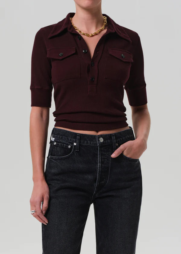 Person wearing a burgundy cropped shirt and black jeans on a plain background