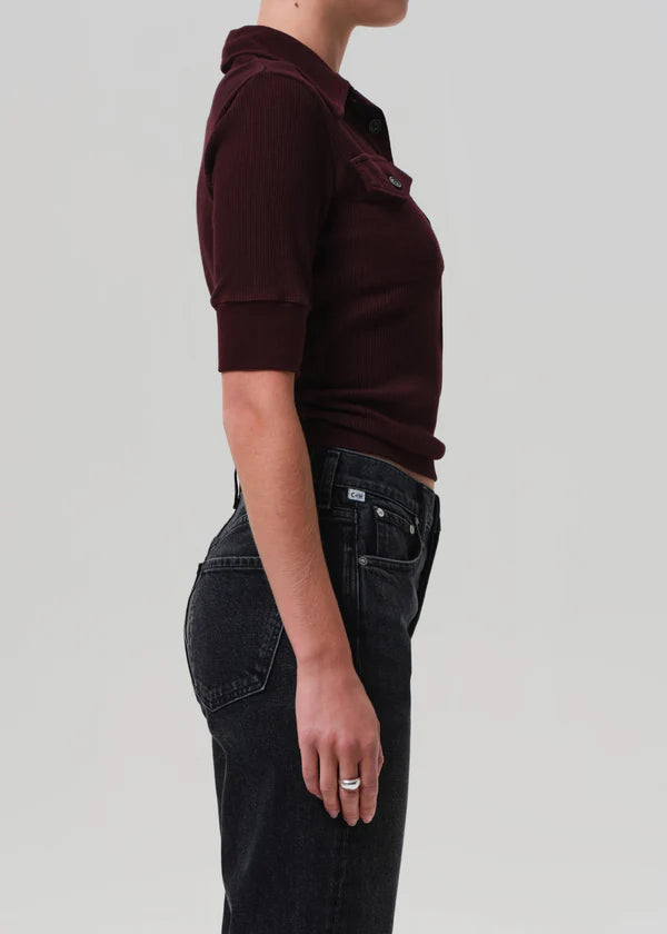 Person wearing a maroon shirt and black pants on a plain background side view