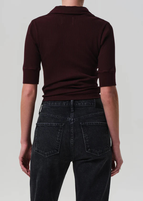 Person wearing a dark brown polo shirt and black jeans on a light gray background back view