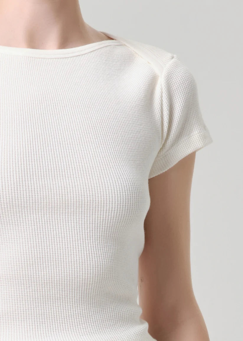 Close-up of a person wearing a short-sleeve waffle-knit top in a warm off-white or cream color, shown against a light gray studio background.