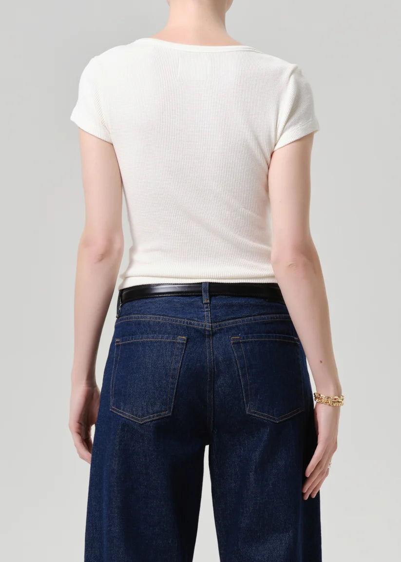 A model shown from the back wearing a fitted off-white short-sleeve t-shirt and dark blue wide-leg jeans with a black belt, against a light gray studio background.