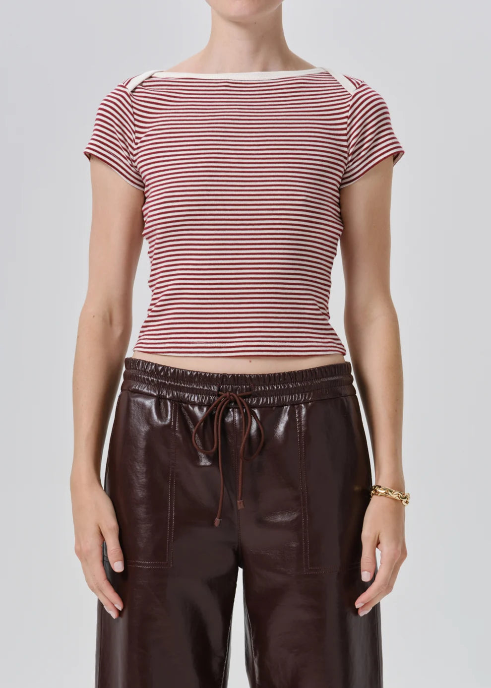 A model wearing a burgundy and white striped short-sleeve top with dark brown faux-leather wide-leg pants, photographed against a light gray studio background.