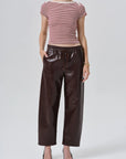 A model wearing a burgundy and white striped short-sleeve top with dark brown faux-leather wide-leg pants and black pointed-toe heels, photographed against a light gray studio background.
