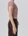 Side profile of a model wearing a short-sleeve cropped top with thin red and white horizontal stripes, paired with dark brown pants, against a light gray studio background.