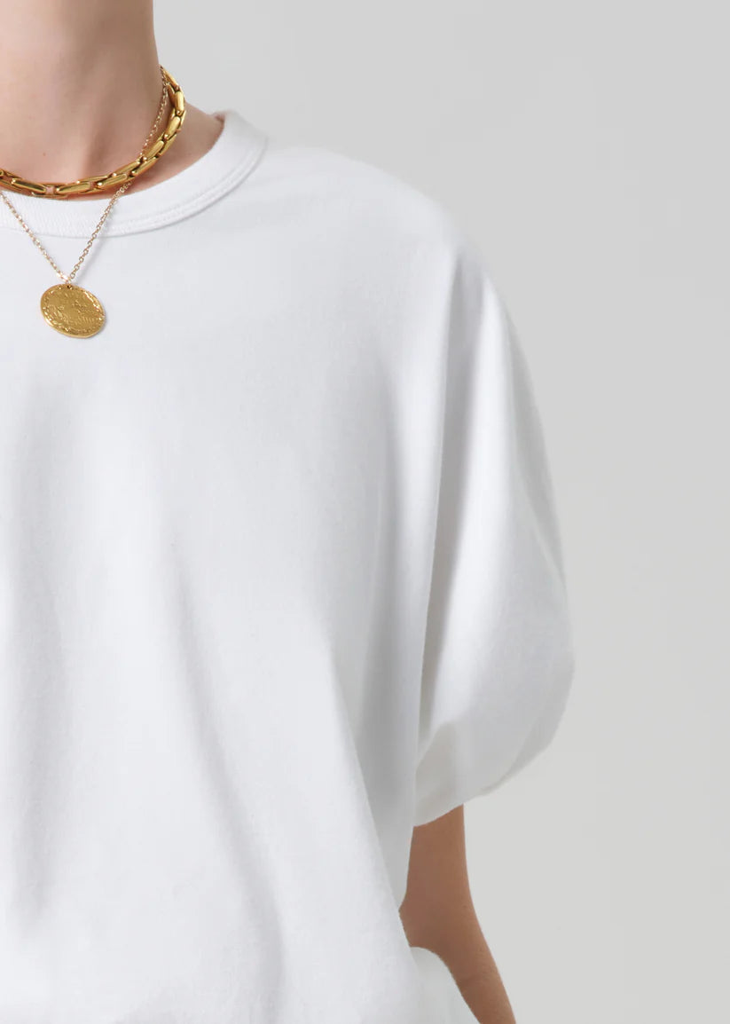 White t-shirt worn by a person with gold necklaces on a light gray background