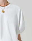 White t-shirt worn by a person with gold necklaces on a light gray background