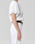 Person wearing a white outfit with a belt on a plain background