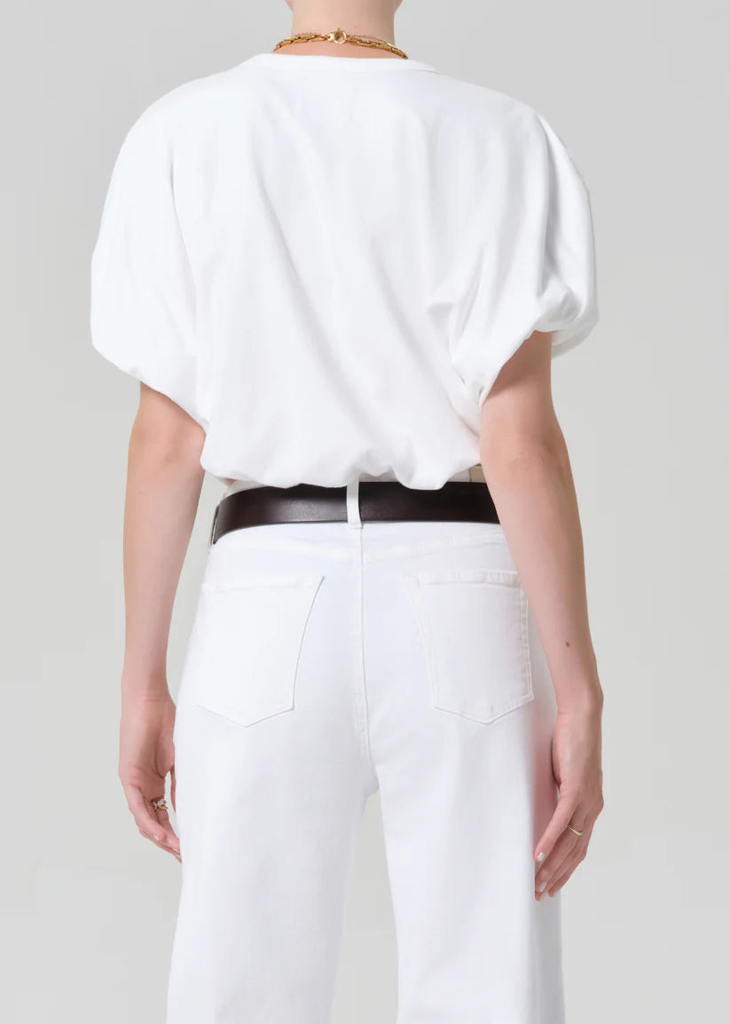 Person wearing a white blouse and white pants with a black belt on a plain background