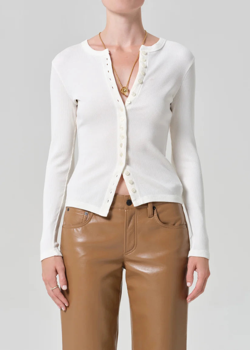 Person wearing a white cardigan and brown pants on a gray background